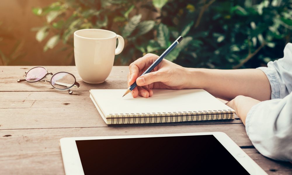 Young business woman hand with pencil writing on notebook. Woman hand with pencil writing on notebook and working at coffee shop.